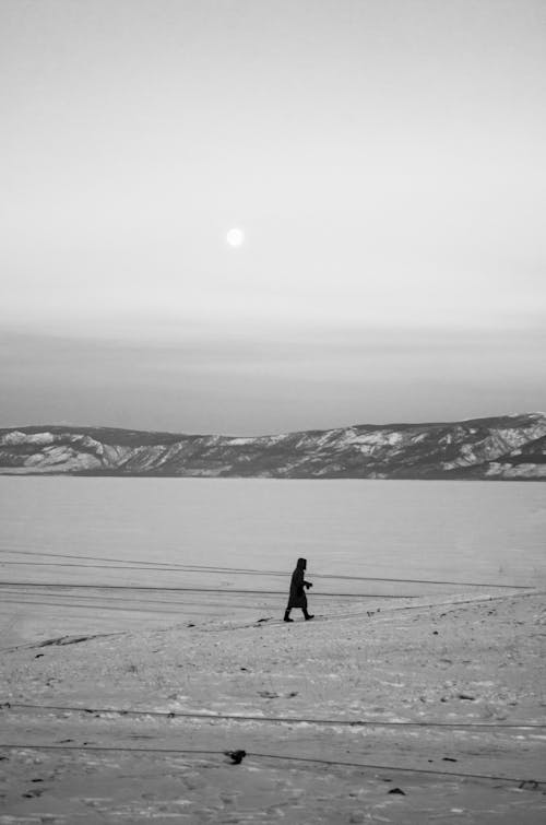 Grayscale Photo of a Person Walking on Snow-Covered Ground