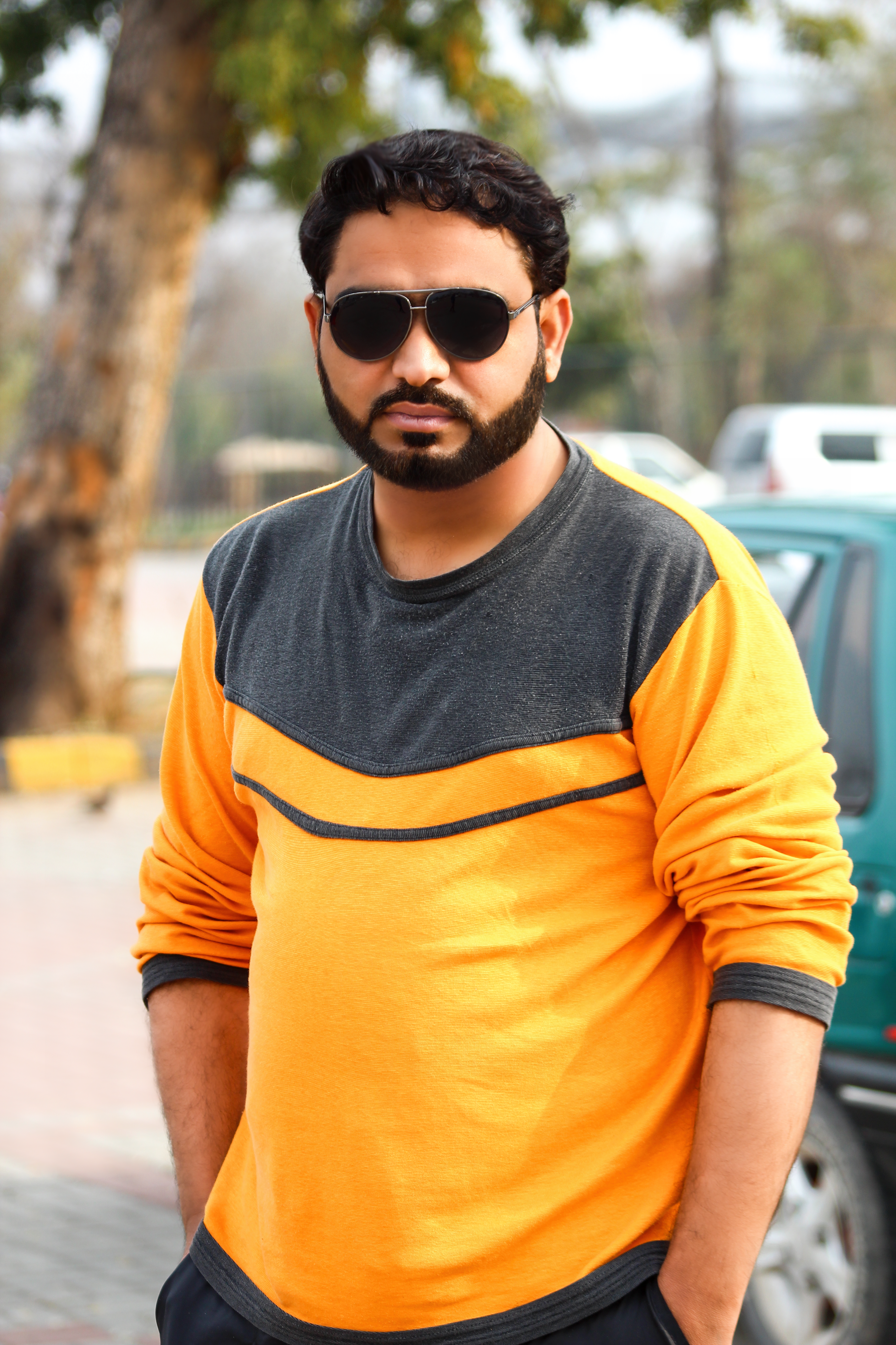 A confident man wearing sunglasses and an orange sweater, posing outdoors.