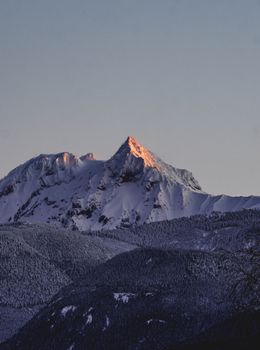 Captivating view of snow-covered mountain peak at sunrise with clear sky.
