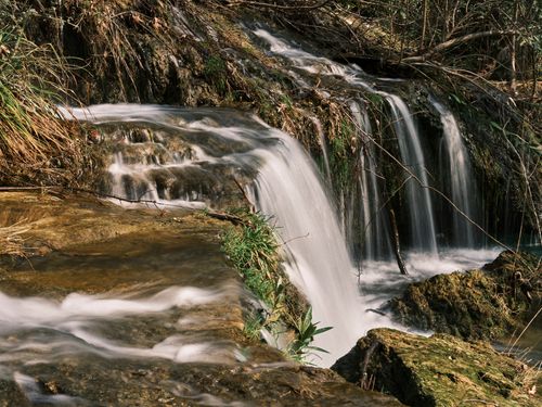Free Peaceful waterfall cascading over rocks surrounded by greenery in a tranquil forest. Stock Photo