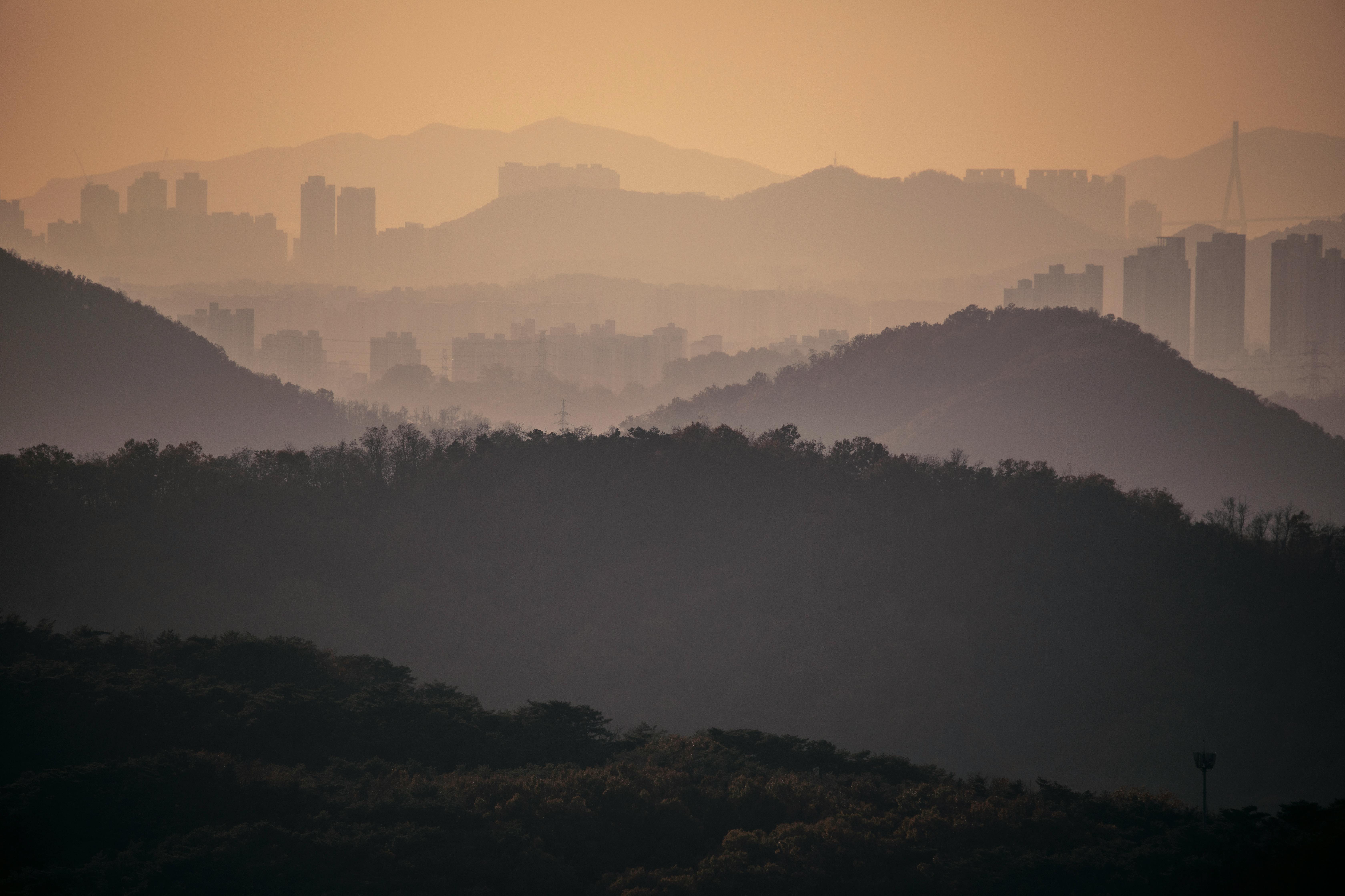 Dramatic view of Seoul mountains silhouetted against a misty sunset, capturing urban and natural harmony.