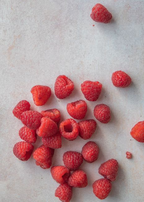 A close-up of ripe, fresh raspberries scattered on a light concrete surface.
