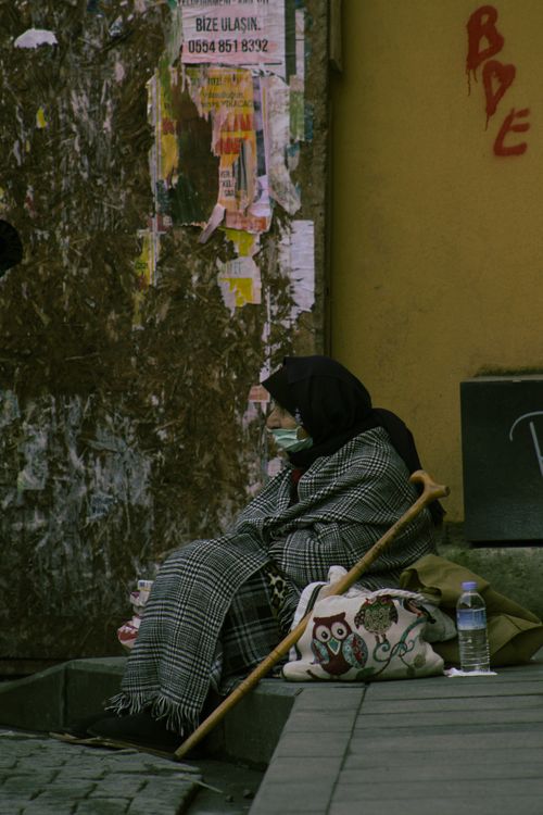 Free A thoughtful moment captured of an elderly woman in Turkey, wrapped in a blanket and sitting on a street corner. Stock Photo