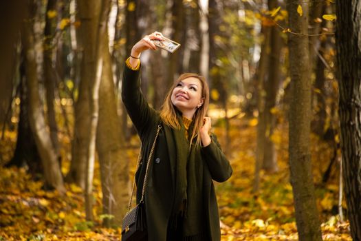 Cheerful woman capturing a selfie amidst the colorful autumn forest in Moscow.