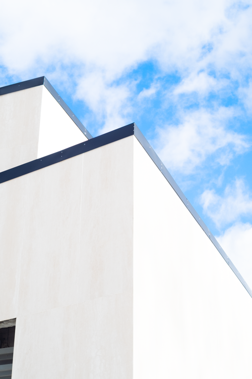 Free A minimalist facade contrasts sharply with a vibrant blue sky and clouds. Stock Photo