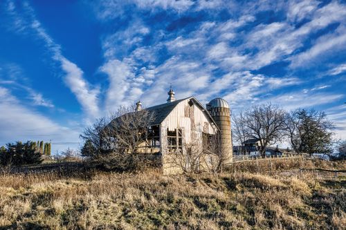 Free A scenic view of an abandoned farmhouse and barn under a vibrant blue sky in Minnesota. Stock Photo