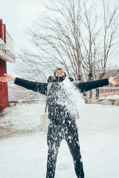 A man joyfully throws snow into the air, embracing the winter season outdoors.