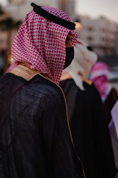 Close-up of an adult wearing traditional Saudi attire, featuring a red and white kaffiyeh and black mask.
