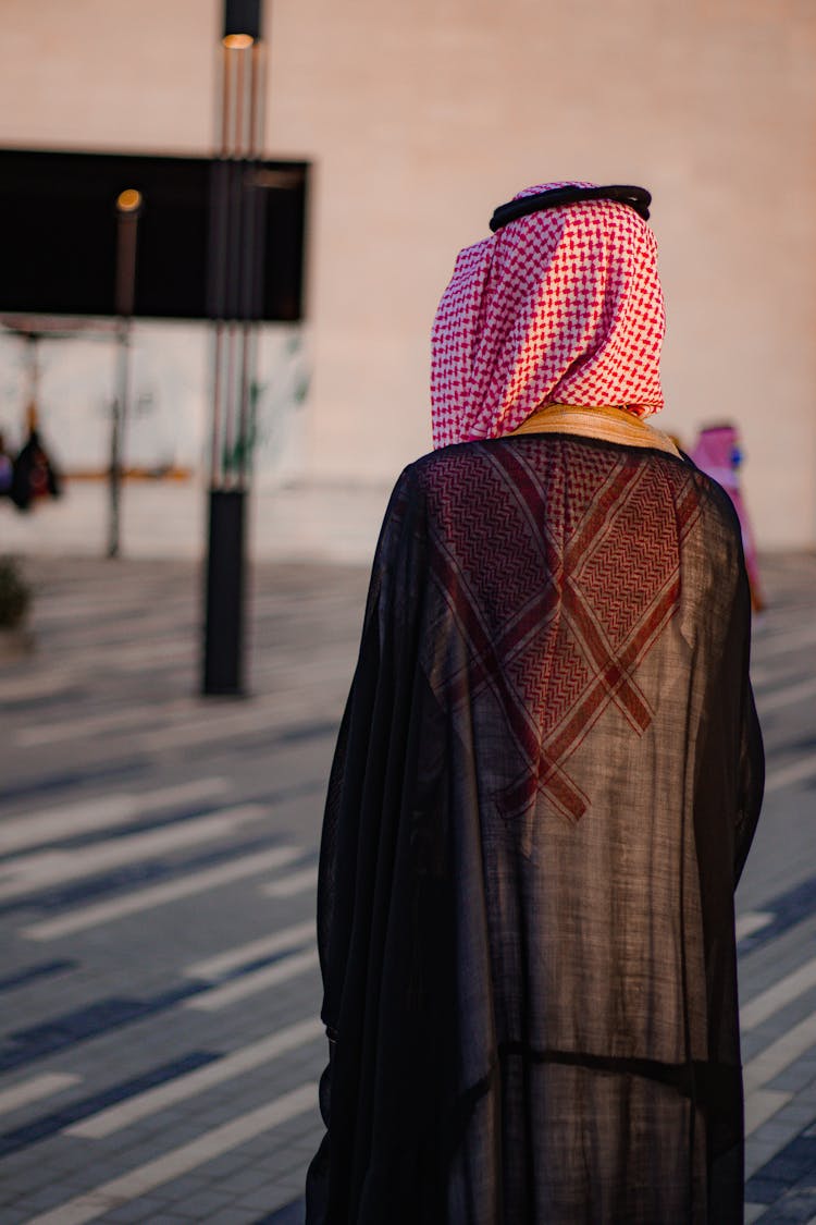 A Person Standing In Black Robe Wearing Kaffiyeh