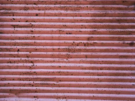 Close-up of a weathered pink corrugated metal surface with rust and dirt.