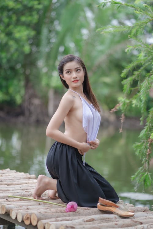 A Woman in White Tank Top and Black Skirt Posing on Bamboo Dock