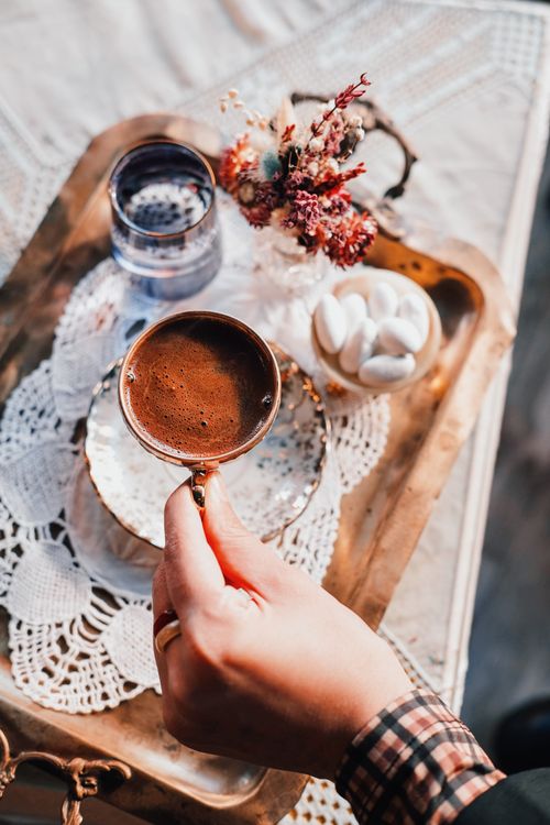Free A hand holding a cup of coffee on a decorative tray with lace, flowers, and sweets. Stock Photo
