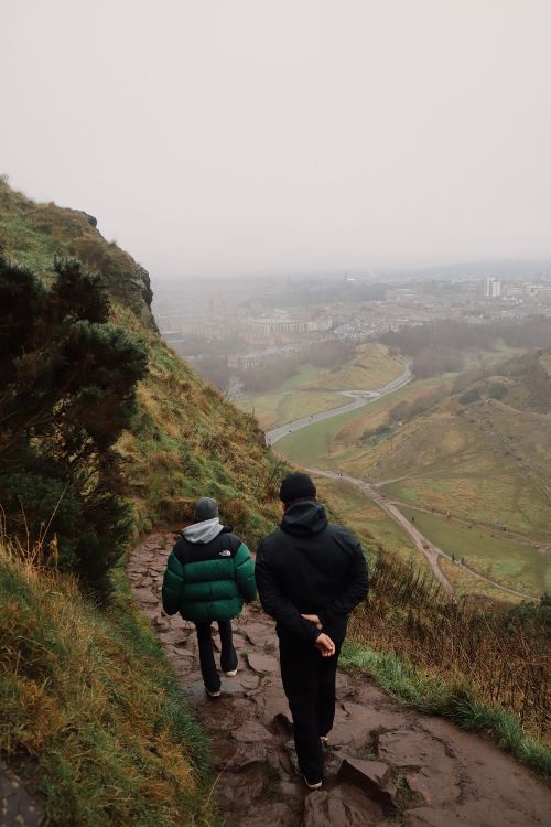 Free Two people hiking down a misty mountain trail overlooking a city's landscape. Stock Photo
