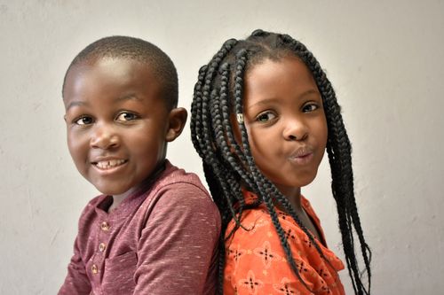Free Close-up portrait of two smiling African children posing back to back indoors. Stock Photo