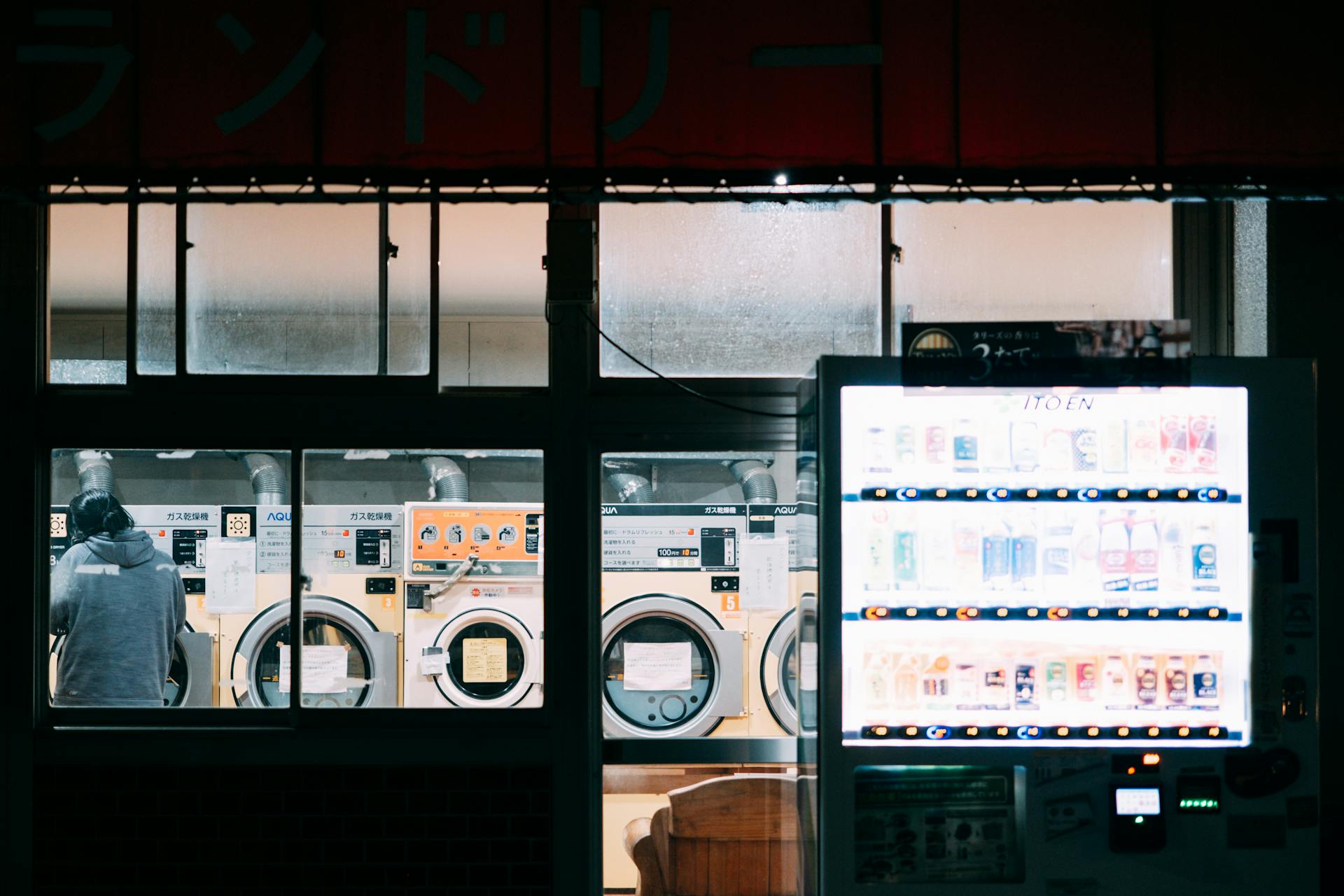 A cozy nighttime scene at a laundry shop with a bright vending machine and washing machines.
