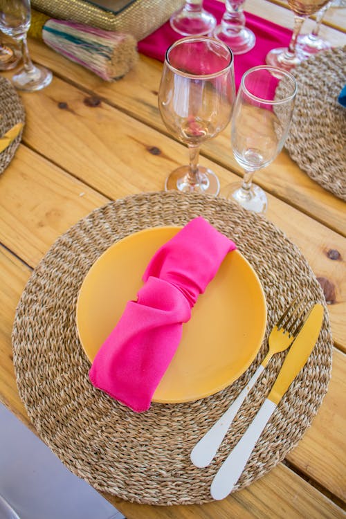Free Braided Place Mats, Yellow Tableware, and Pink Napkins on a Wooden Table Stock Photo