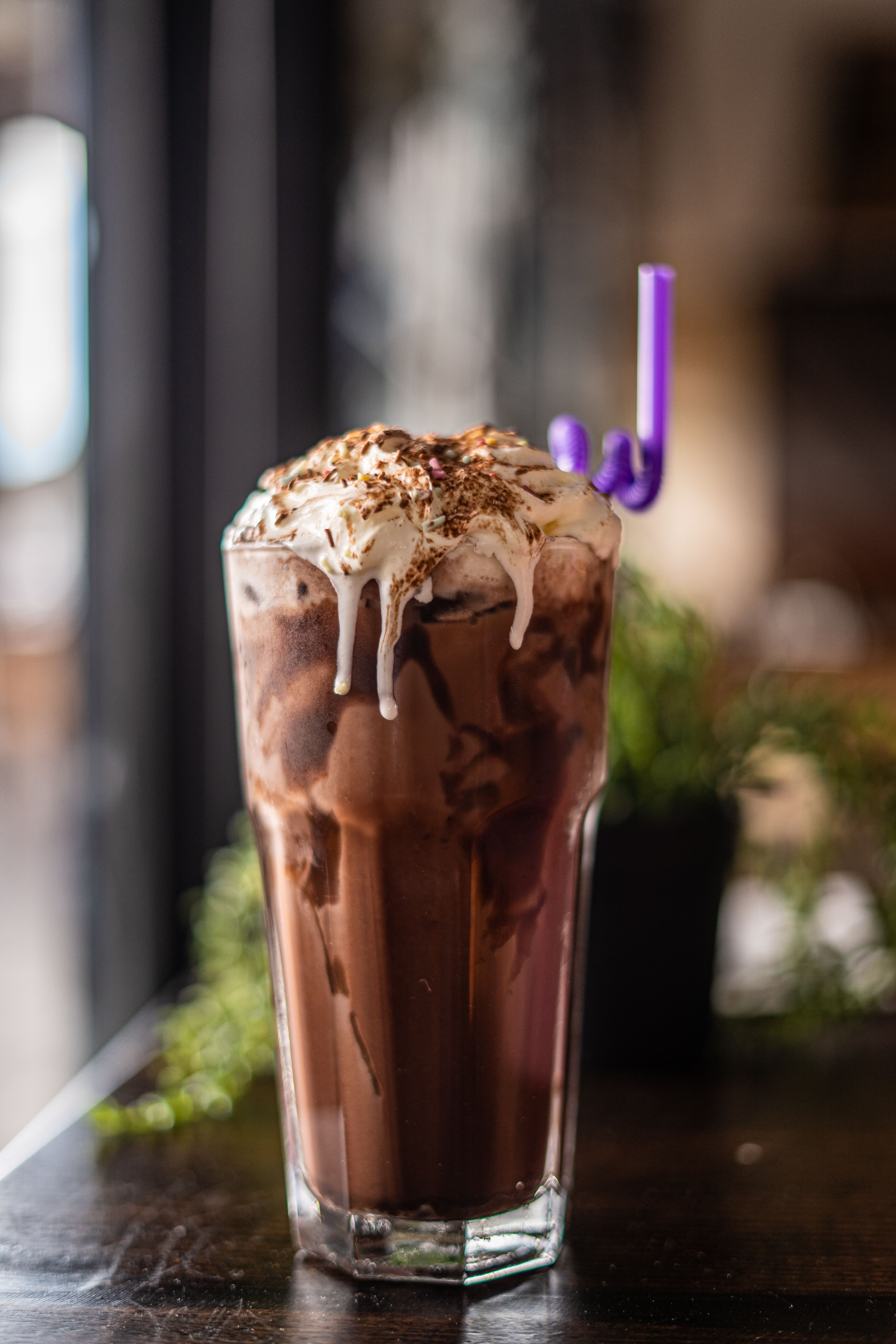 Close-up of an iced chocolate drink topped with whipped cream and chocolate flakes in a tall glass.