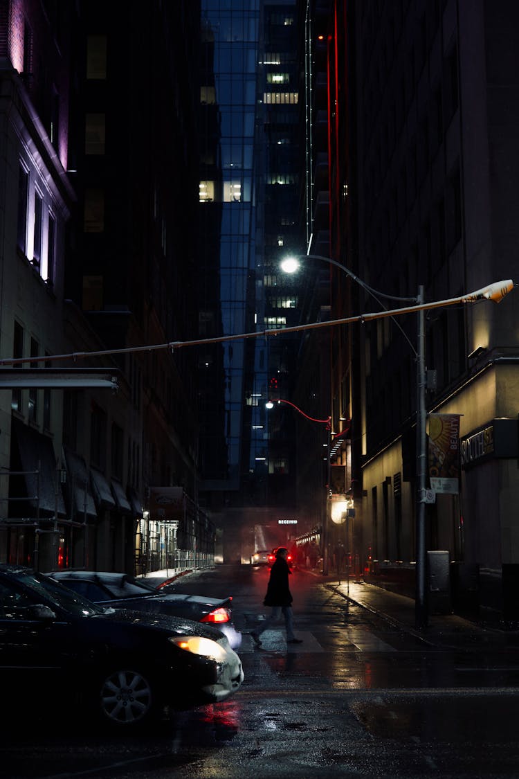 A Person In Red Jacket Walking On Street During Night 