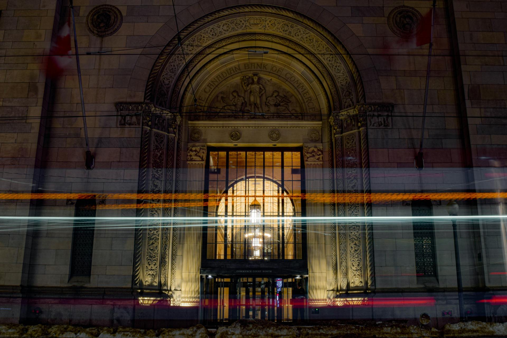 A nighttime long exposure capturing light trails in front of a historic bank facade with intricate architecture.