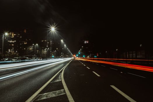 Captivating long exposure of city street at night showing dynamic light trails from vehicles under streetlights.