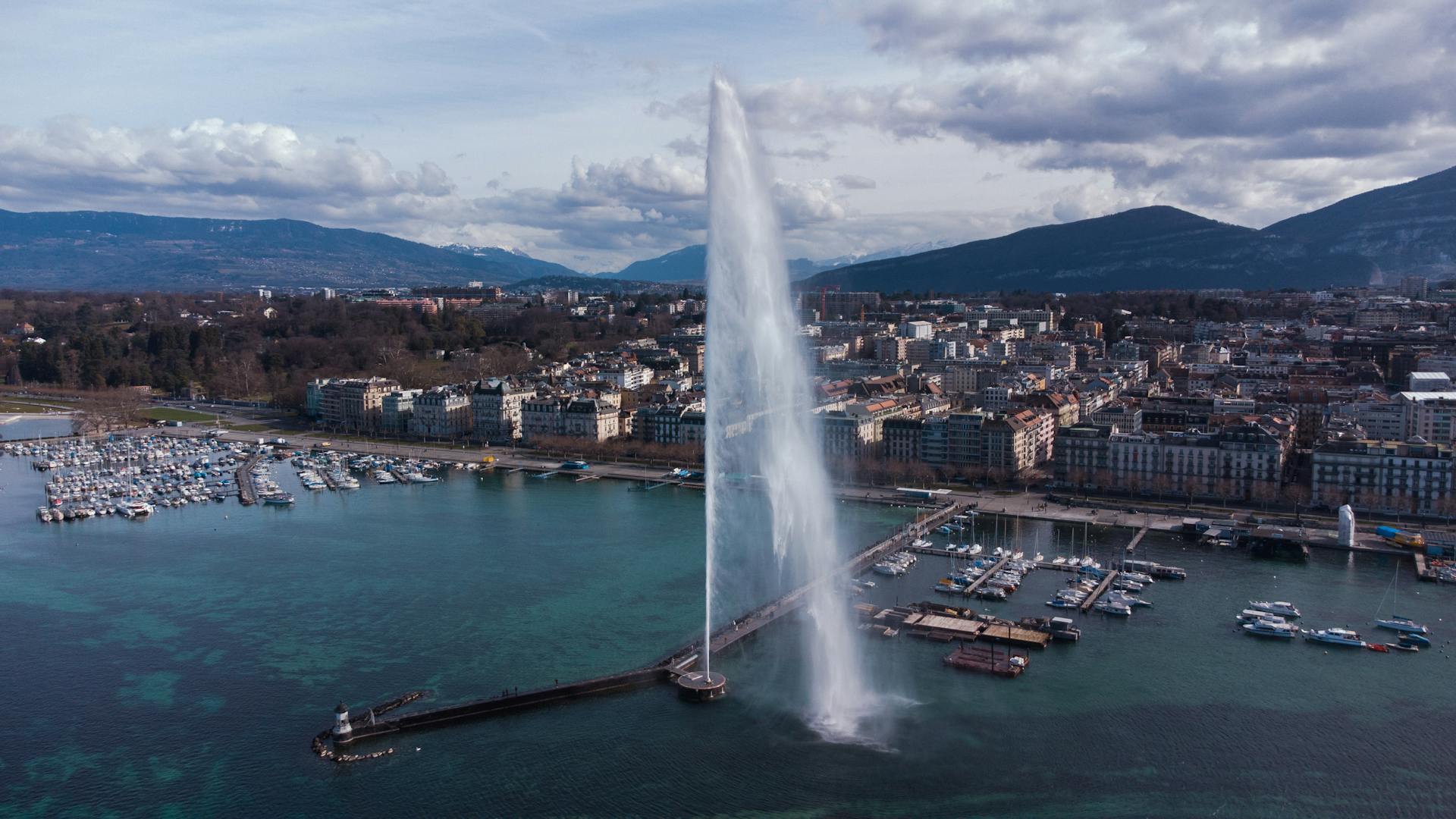 Stunning aerial view of Jet d'Eau fountain and Geneva cityscape against mountainous backdrop.