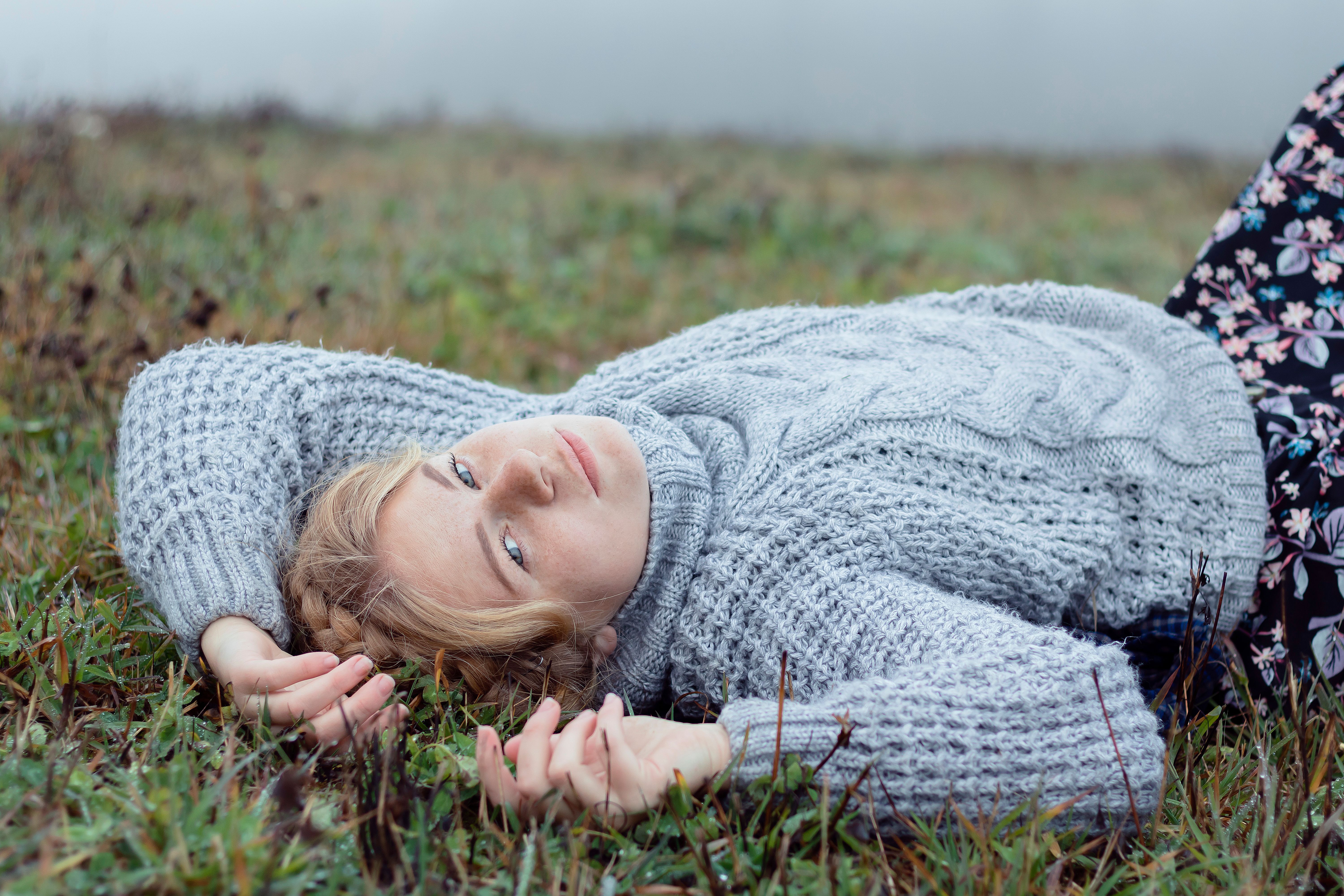 Young woman in a knitted sweater lies on grass, looking at the camera.
