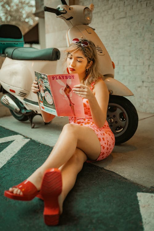 Free Woman Sitting Next to Motor Scooter and Reading Playboy  Stock Photo