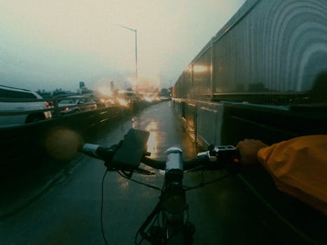 Cyclist navigating a wet bike lane in rainy New York City with blurred traffic lights.