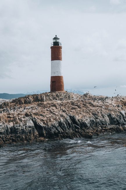 Lonely lighthouse stands strong on rugged rocky shore under an overcast sky.