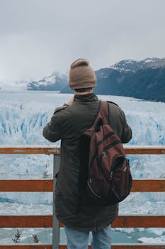 A man in winter clothing photographing a vast snow-covered glacier landscape.