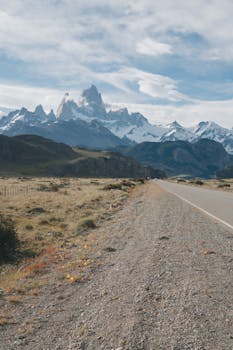 Breathtaking view of a road leading to majestic snowcapped mountains under a cloudy sky.