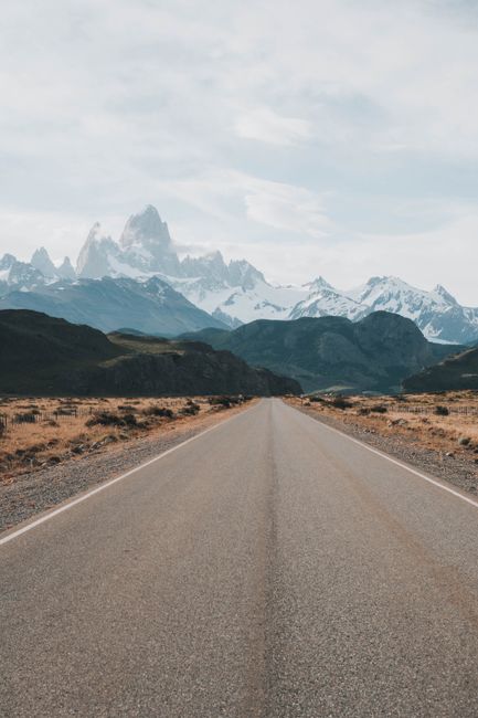 Long road stretching towards snow-capped mountains under a clear sky.