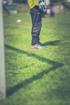 Goalkeeper standing on green field, focused on legs with gear, during a sunny day soccer match.