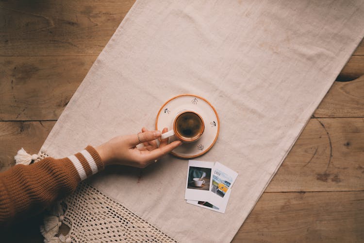 Unrecognizable Female Hand Reaching For Cup Of Coffee On Table