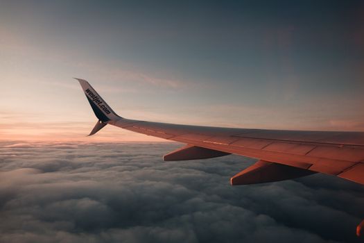 A breathtaking view of an airplane wing during a flight above clouds at sunset, capturing serene beauty.