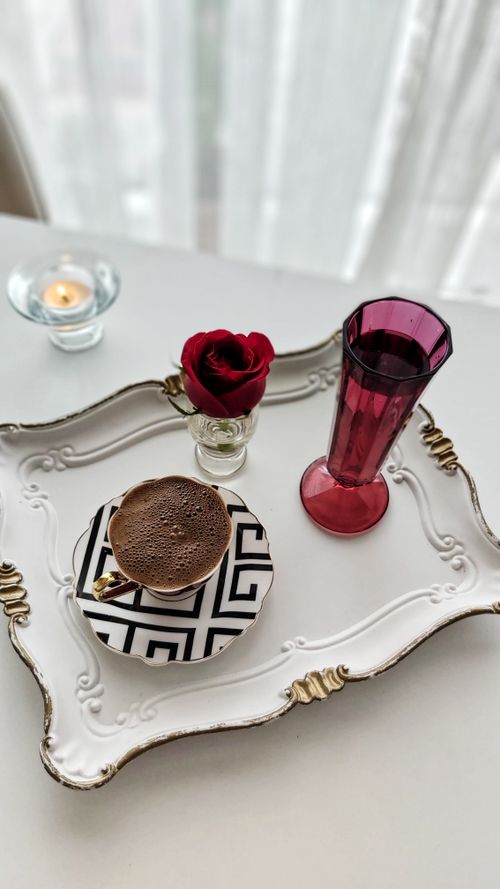 Free A stylish coffee setup featuring a cup, red rose, and candle on a decorative tray. Stock Photo