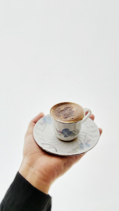 Free A hand holding an elegant coffee cup with saucer on a white background, showcasing simplicity and tranquility. Stock Photo