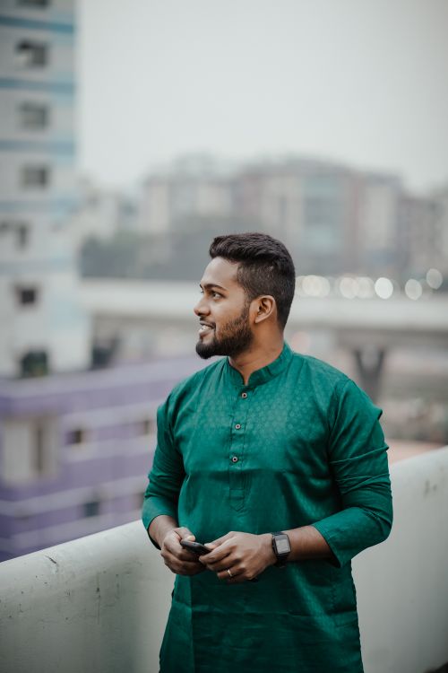 Free Portrait of a smiling South Asian man in green traditional attire with city background. Stock Photo