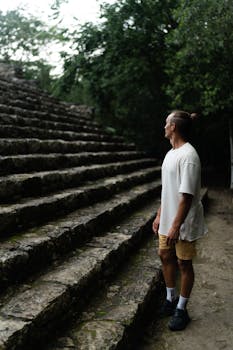 A man stands thoughtfully by ancient ruins in Coba, Mexico amid lush greenery.