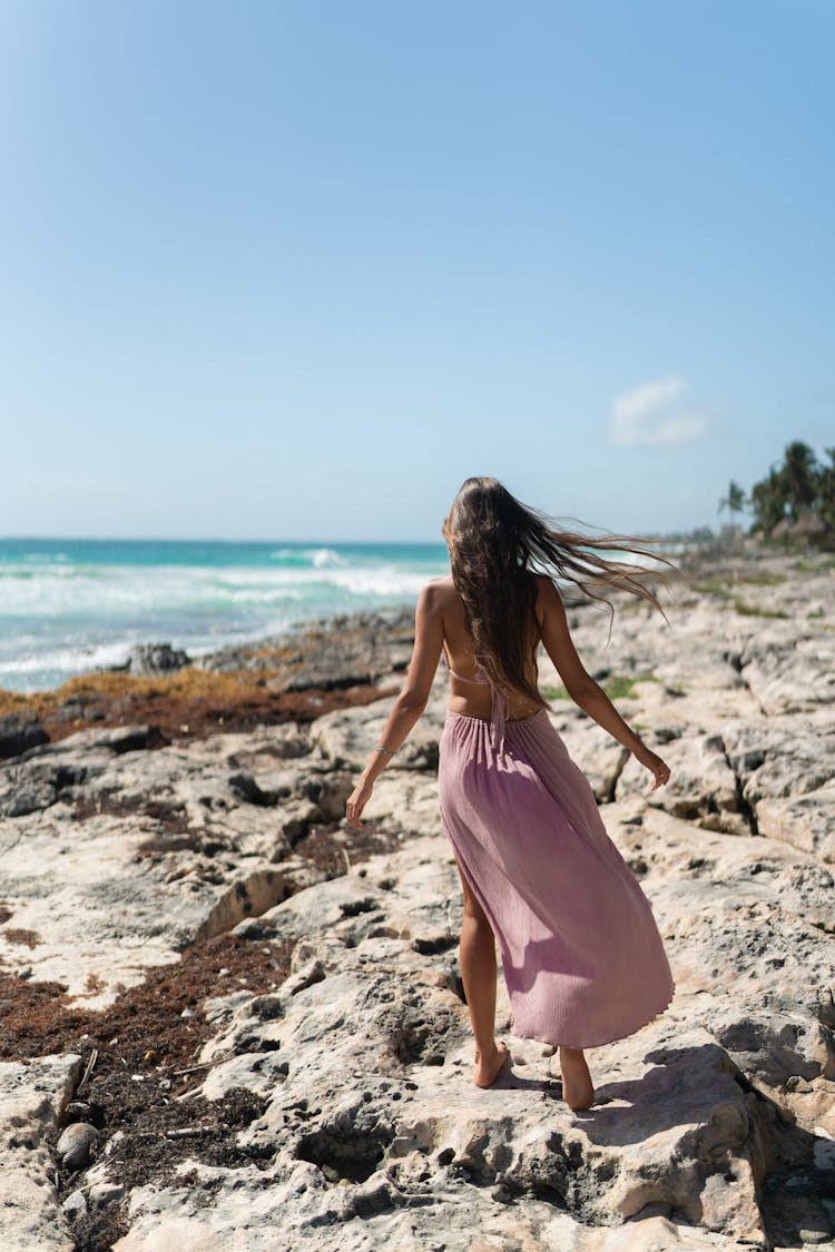 A Person In Purple Dress Walking On The Rocky Shore