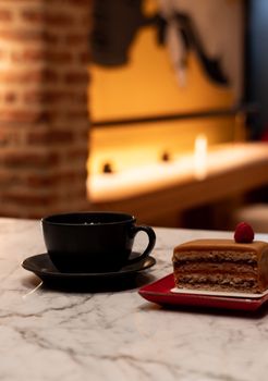 Stylish black coffee cup and sliced dessert on a marble table with soft indoor lighting.