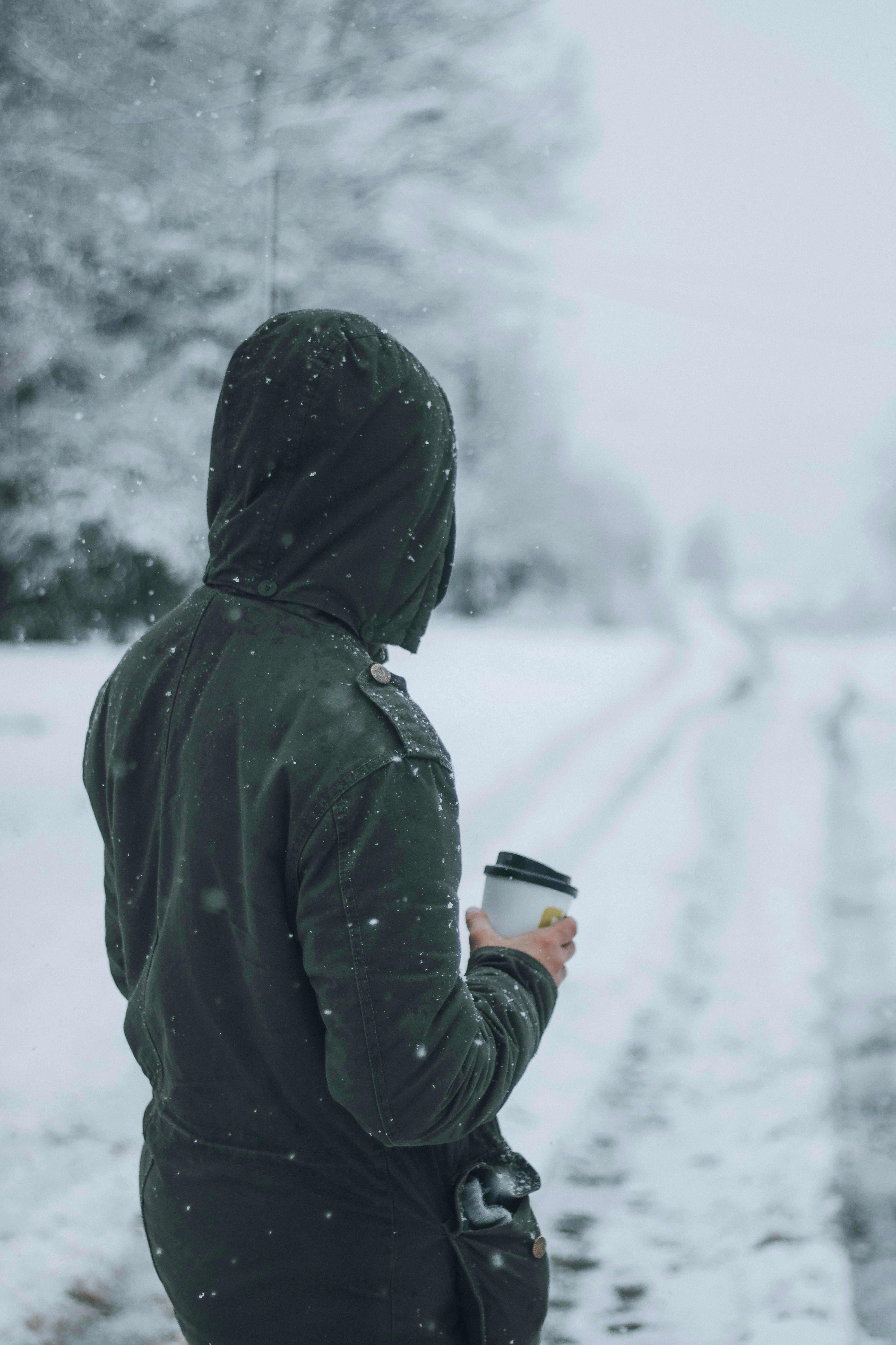 A Man Wearing a Gray Hoodie Holding a Coffee Cup Outside on a Snowy Day ·  Free Stock Photo