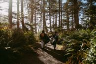 Woman in Black Jacket Walking on Dirt Road Between Trees