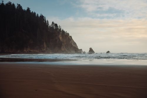 Free Serene beach scene with rocky cliffs and gentle ocean waves under a partly cloudy sky. Stock Photo