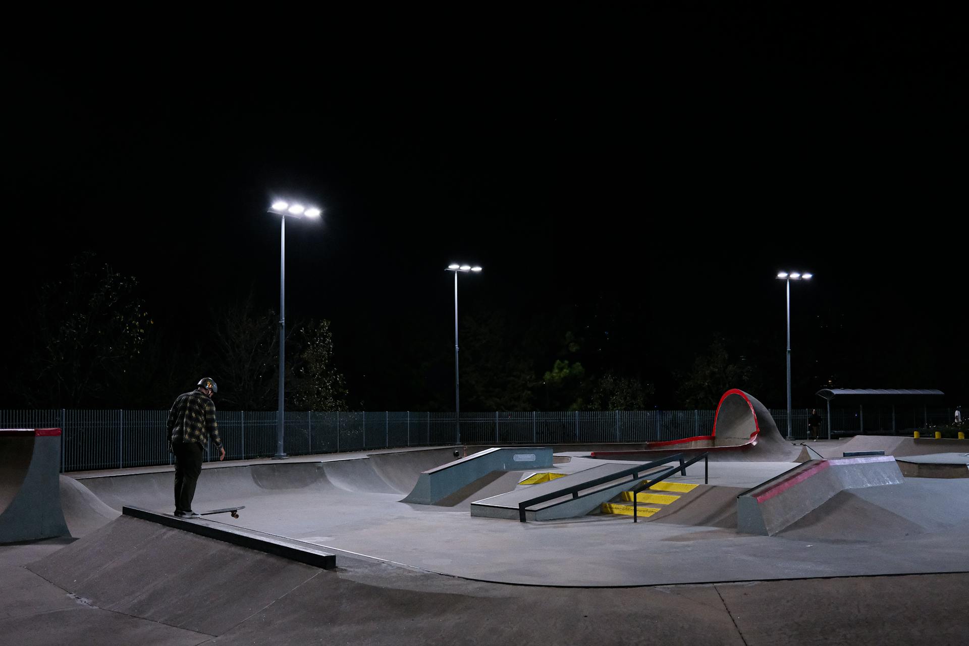 A skateboarder practices at a lit skate park in Houston at night.