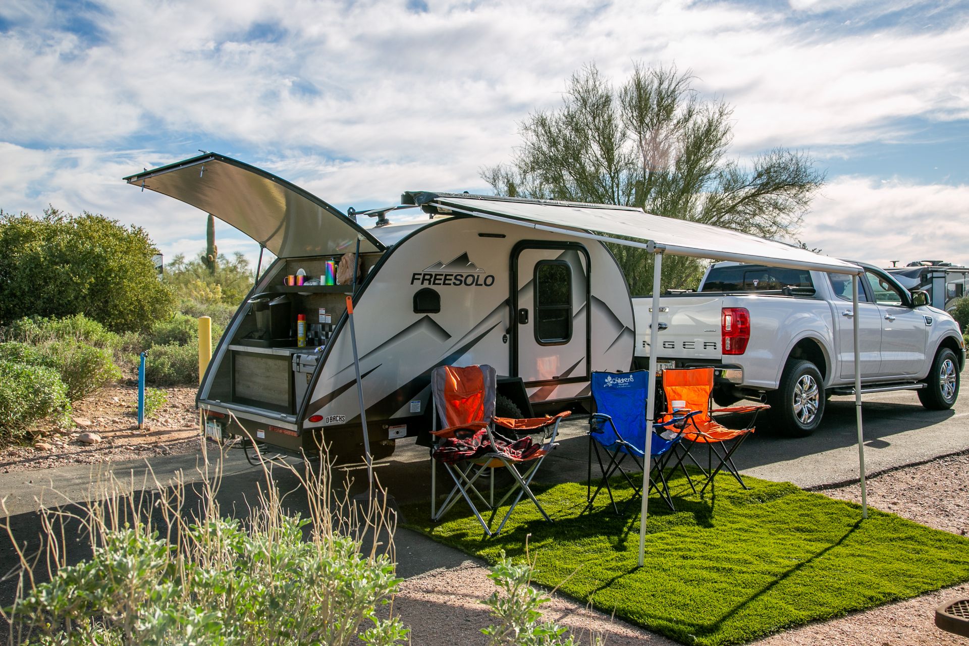 A scenic campsite in Apache Junction, AZ showcasing a Freesolo motorhome with camping chairs and pickup truck.