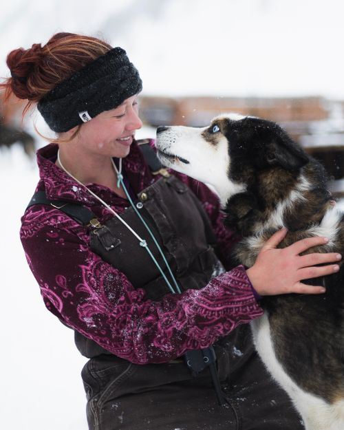 Free Woman in winter attire joyfully hugging a Siberian Husky outside in snowy weather. Stock Photo