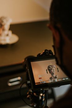 A video camera focuses on a marble head bust sculpture inside a studio setting.