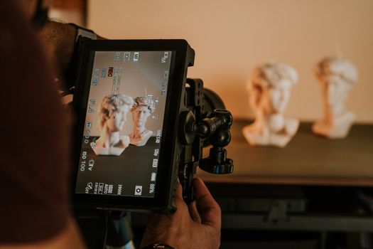 Photographer using camera to capture sculptures in studio setting with focus on digital screen.