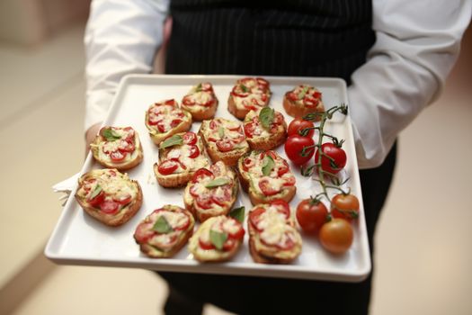 A waiter presents a tray of gourmet bruschetta with fresh tomatoes and basil.